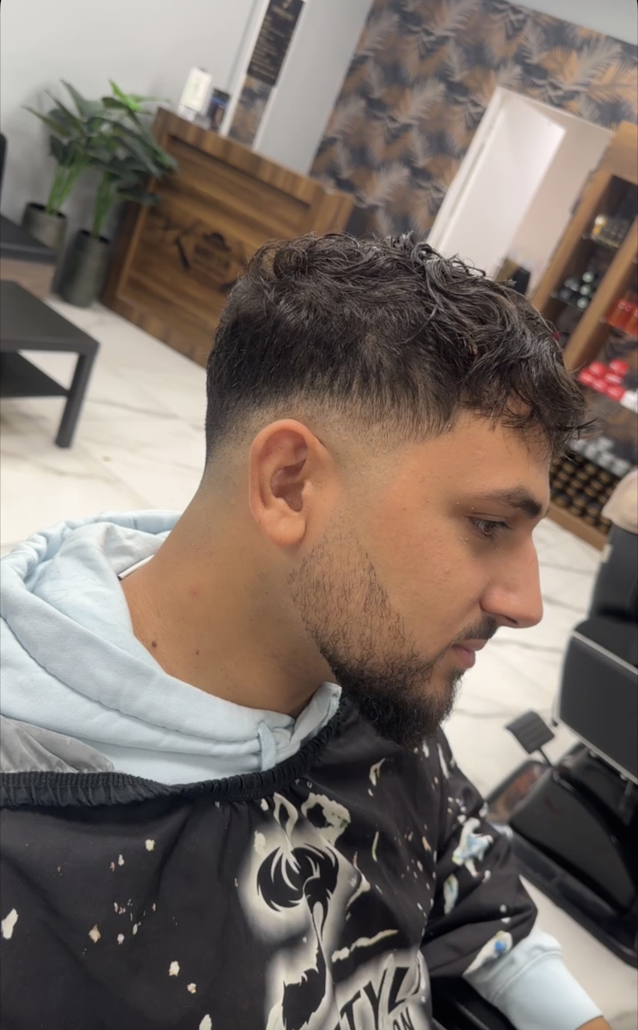 Klant met donkere krullen en een korte fade aan de zijkant, van opzij gezien in de zaak