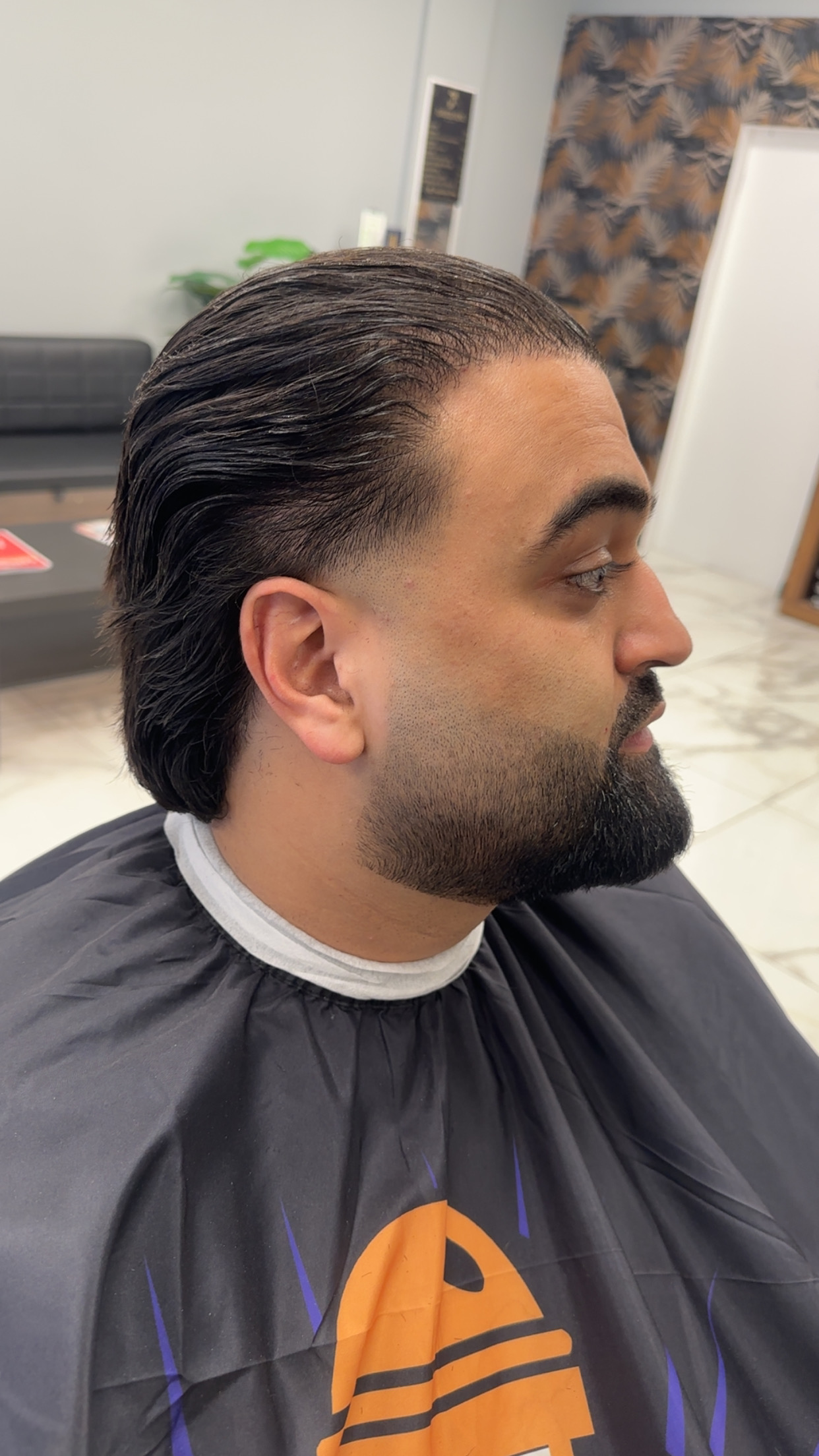 Klant met achterovergekamd haar en een volle, strak bijgewerkte baard, van opzij gezien in de zaak