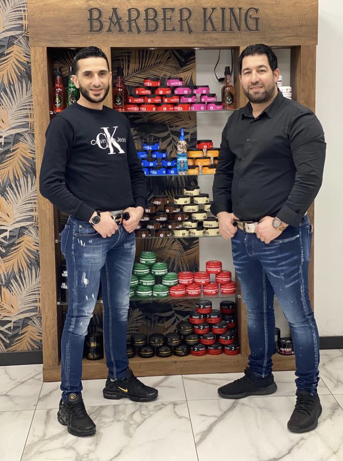 Twee kappers voor de houten productwand met het bord Barber King