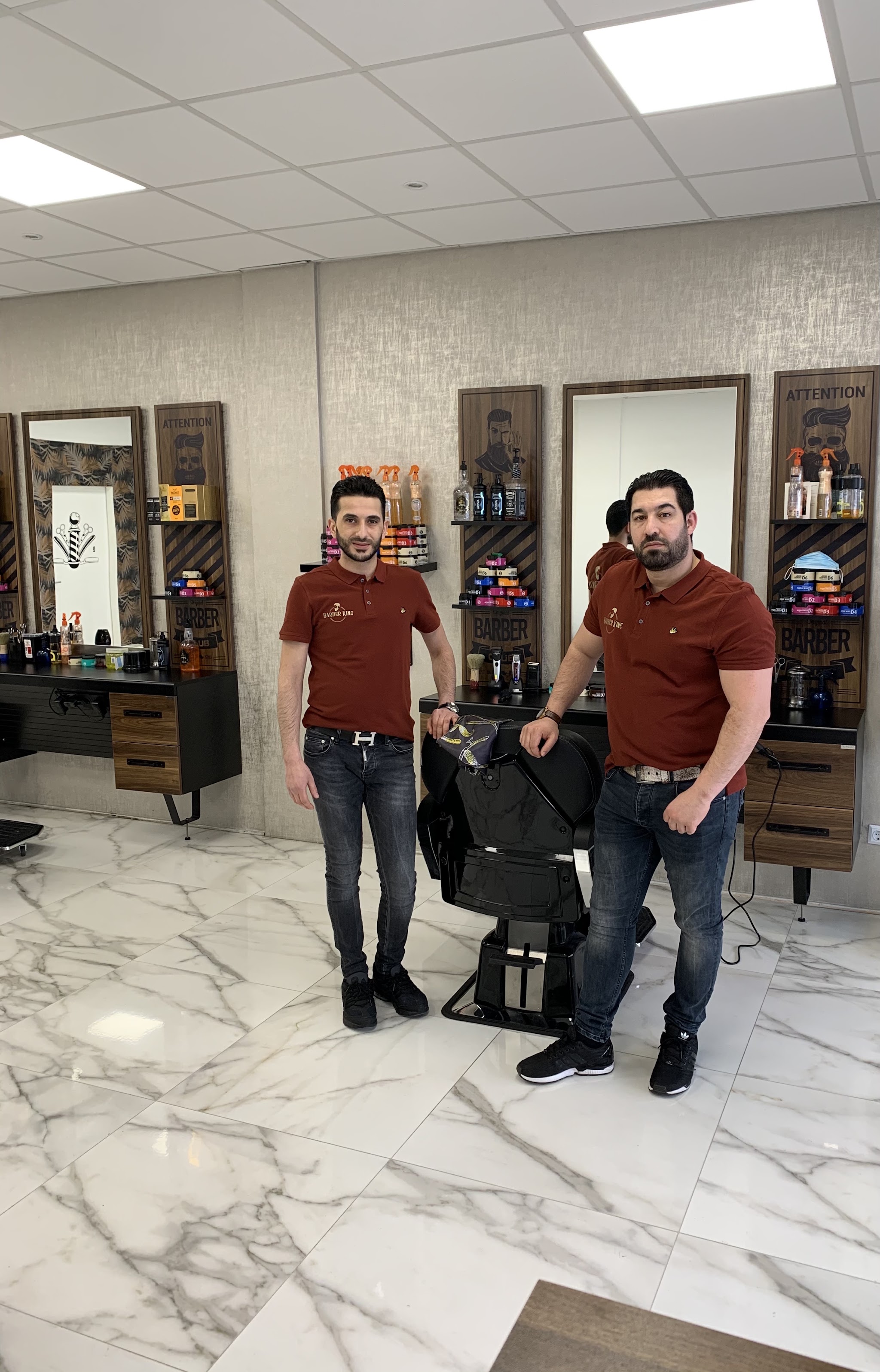 Twee kappers van Barber King in rode shirts in de zaak, tussen de spiegels en de kappersstoelen