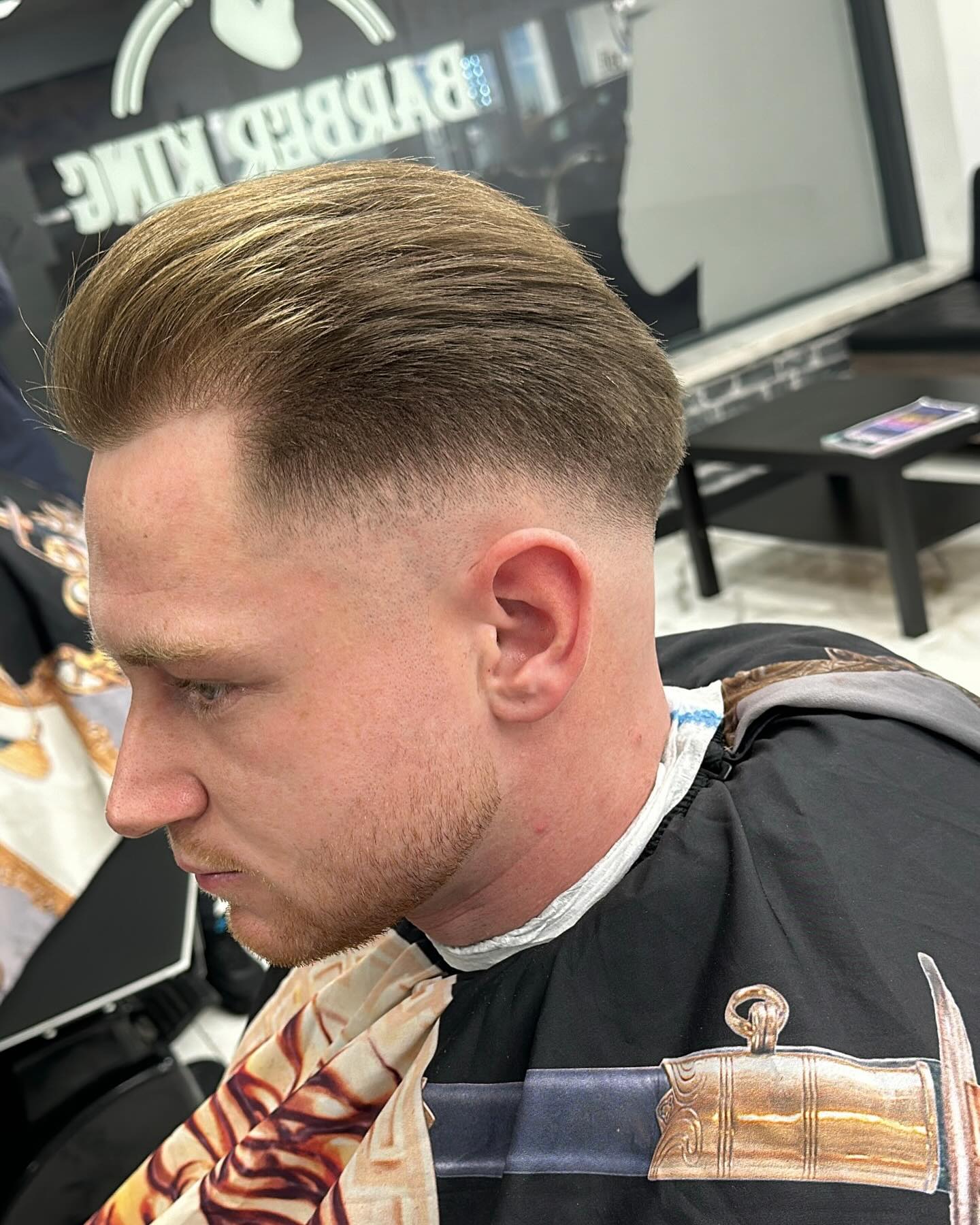 Klant met blond achterovergekamd haar en een fade, van opzij gezien